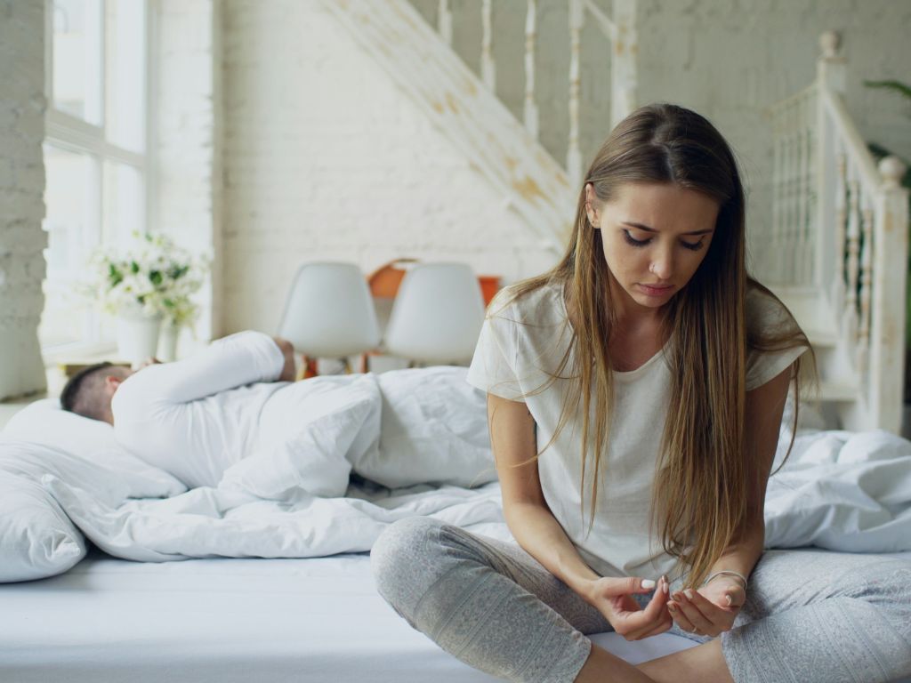 Image of woman sitting on her bed while a man sleeps - divorce singapore