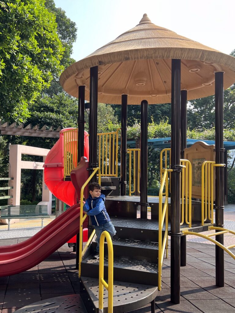 Child climbing a play frame under a thatched shelter at the Hong Kong Zoological and Botanical Gardens