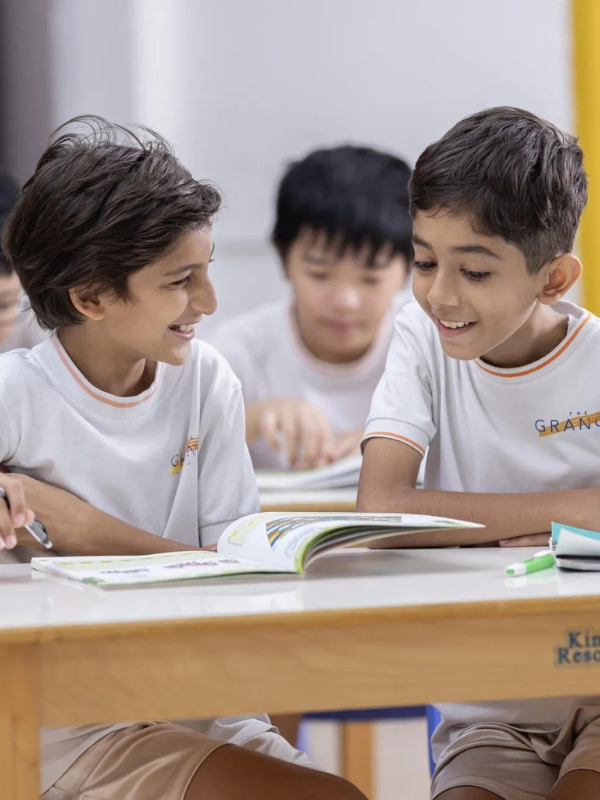 students sitting at a desk looking at a book