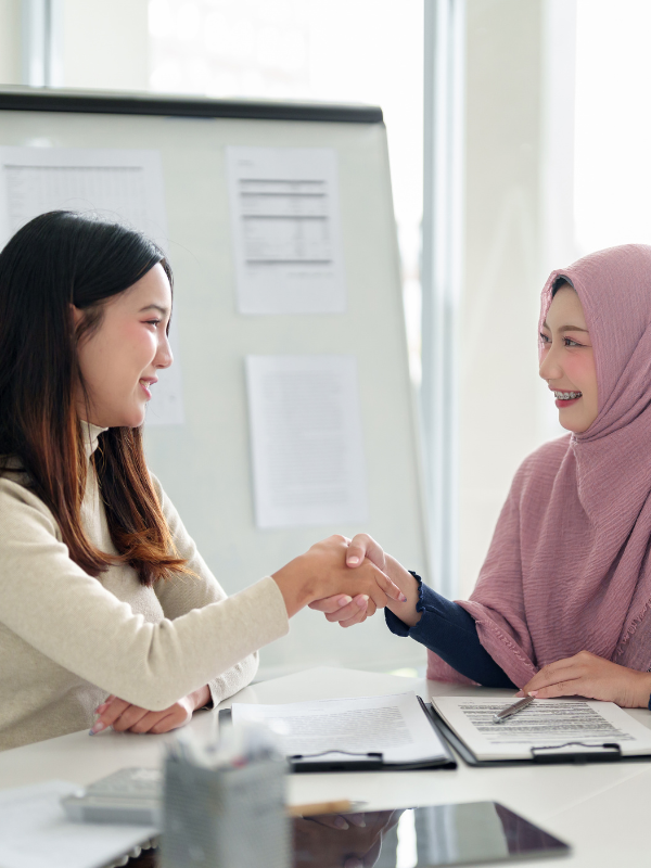 two Asian business women shaking hands in an office setting