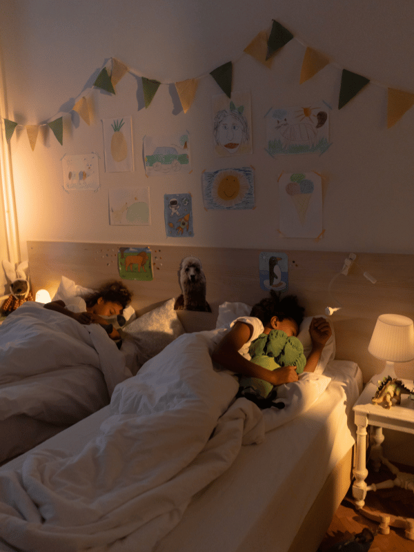 two children sleeping in a darkened room with a night light