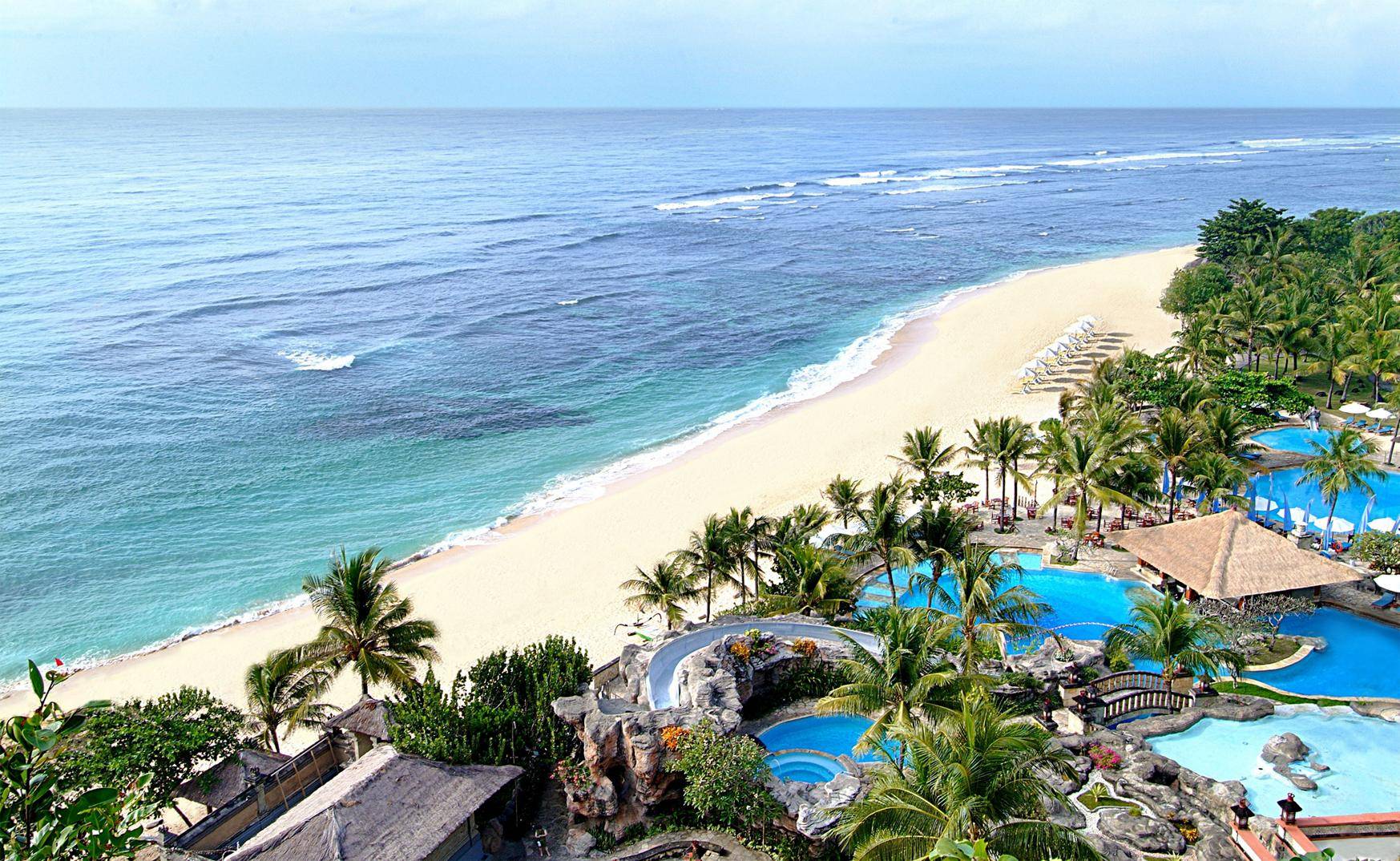 White-sand beach and lagoon pools with a waterslide on Bali's southern coast, palm trees and calm turquoise water