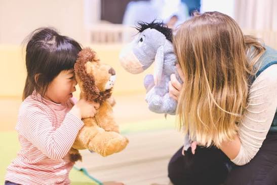 English-speaking babysitter playing with a toddler using a stuffed lion and donkey toy during a kids club session in Niseko