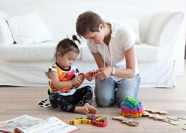 Babysitter from Babysitters and Company with toddler playing with puzzles on the living room floor