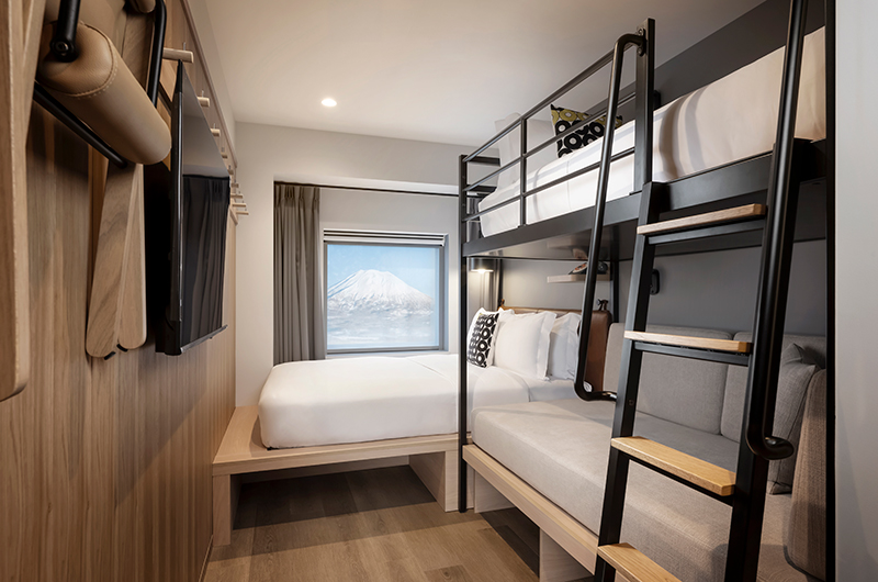 Family loft room at Moxy Niseko Village with a queen bed, bunk bed ladder and snowy Mt Yotei framed in the window