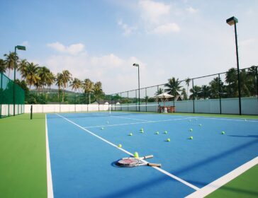 Outdoor hard court with rackets and balls, surrounded by palm trees in Krabi