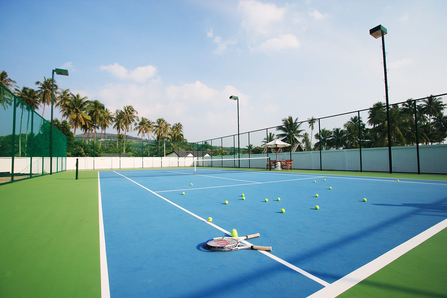 Outdoor hard court with rackets and balls, surrounded by palm trees in Krabi