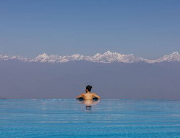 Woman relaxing in the infinity pool at Dwarika’s Sanctuary, Nepal, facing a clear row of snow-capped Himalayan peaks