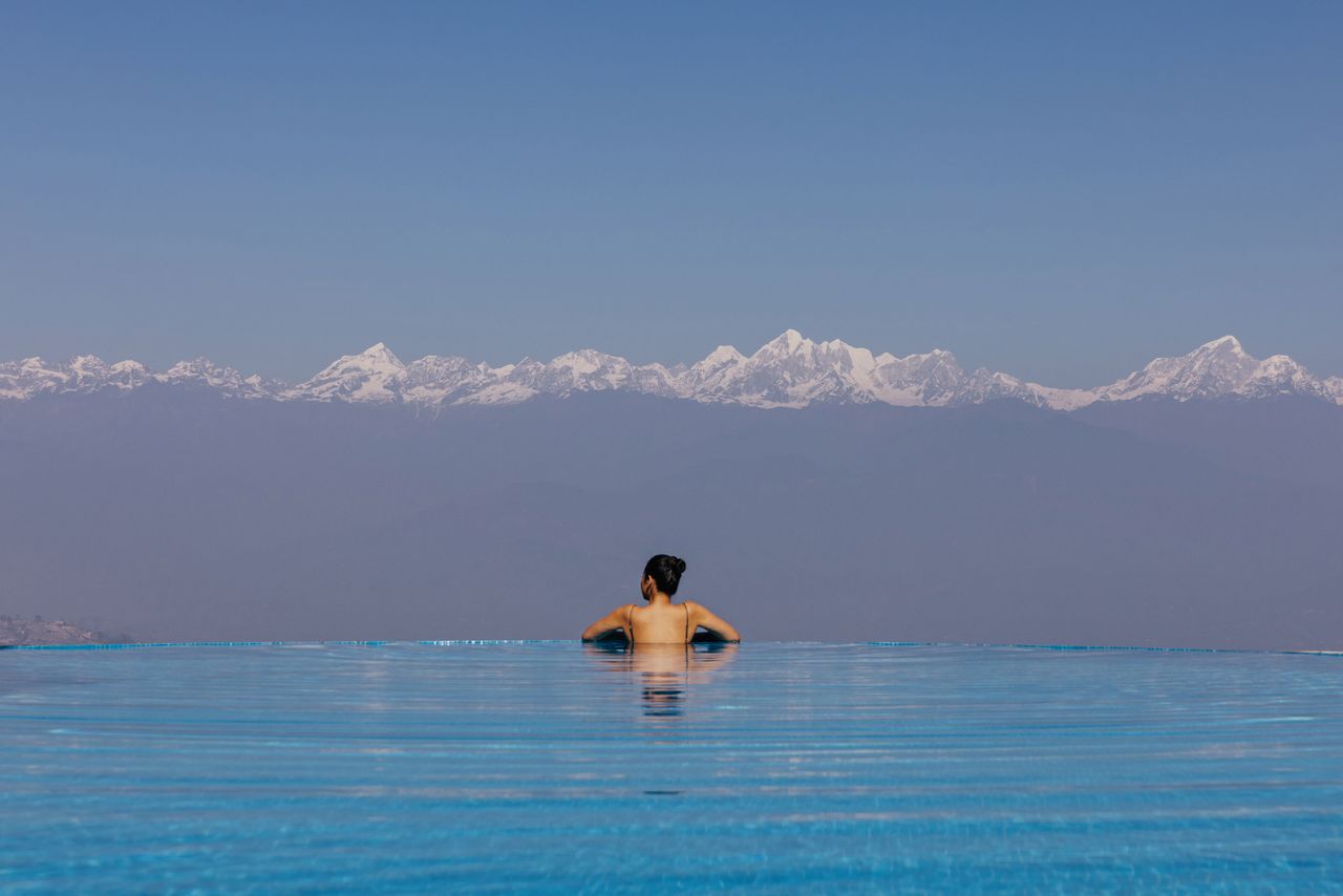 Woman relaxing in the infinity pool at Dwarika’s Sanctuary, Nepal, facing a clear row of snow-capped Himalayan peaks
