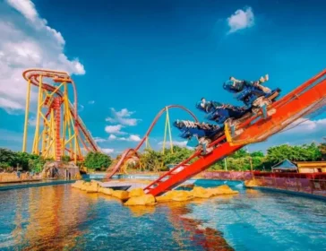 Riders on a dive coaster swooping down towards the water beside looping roller coasters at Chimelong Paradise, Guangzhou