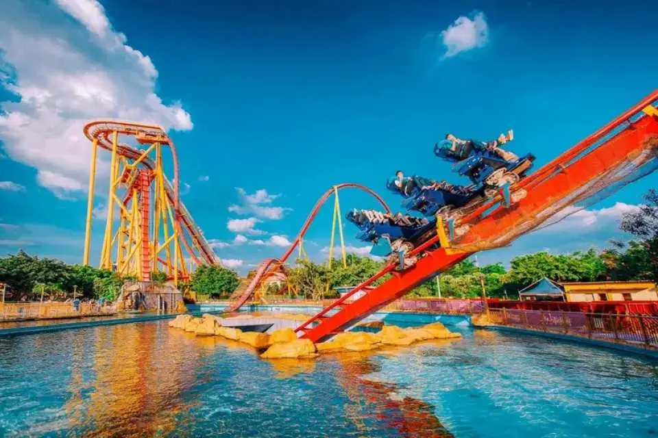 Riders on a dive coaster swooping down towards the water beside looping roller coasters at Chimelong Paradise, Guangzhou